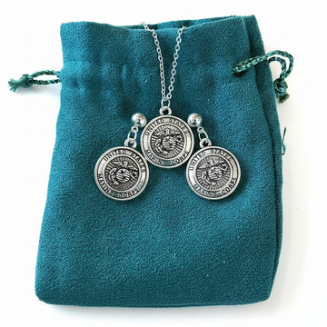 Silver necklace with three round pendants on a teal velvet bag.
