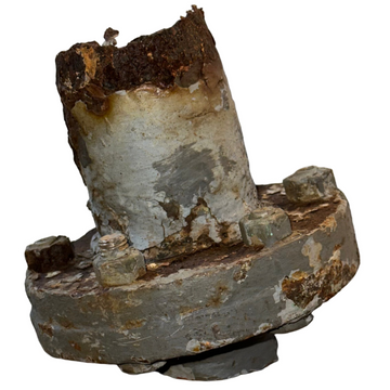 Rust-covered metal component on a concrete floor with a white wall background
