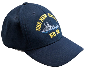 Navy blue cap with USS New Jersey BB 62 logo on a light wooden surface